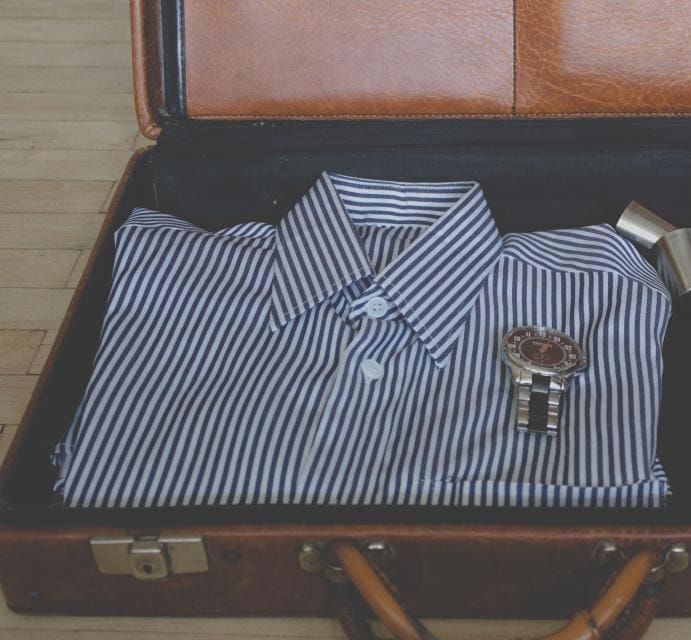 A folded blue-and-white striped shirt and a steel wristwatch packed into an open leather case.