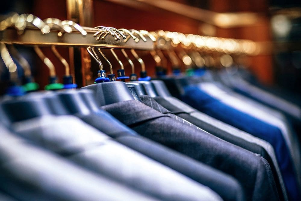 Rows of navy and blue suit jackets hanging on a metal rail under warm store lighting.