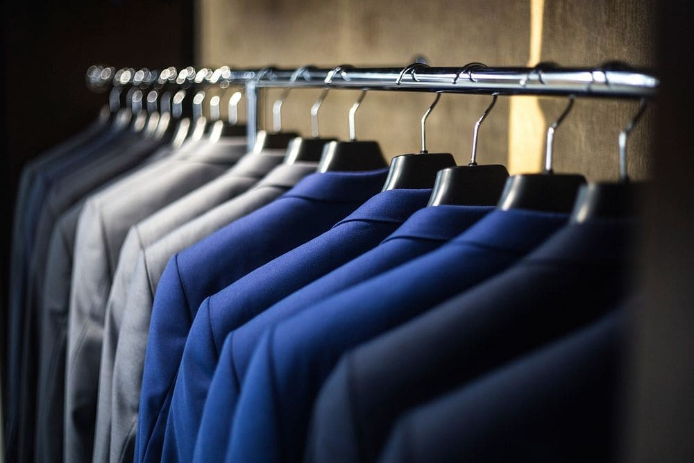 Blue suit jackets lined up on black hangers along a metal rail.
