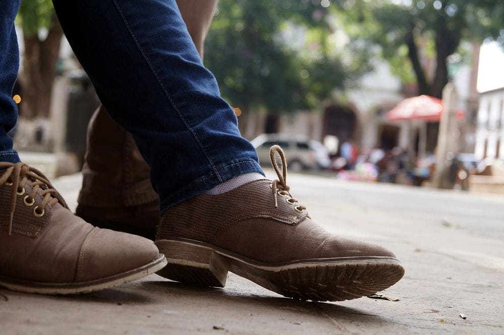 Brown suede two-eyelet desert boots worn with dark jeans on a city sidewalk.